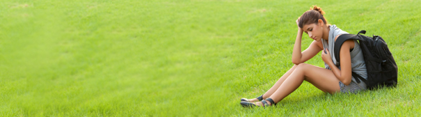 A woman wearing a backpack sitting on a grassy hill.