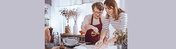 An elderly woman making pies with a young woman